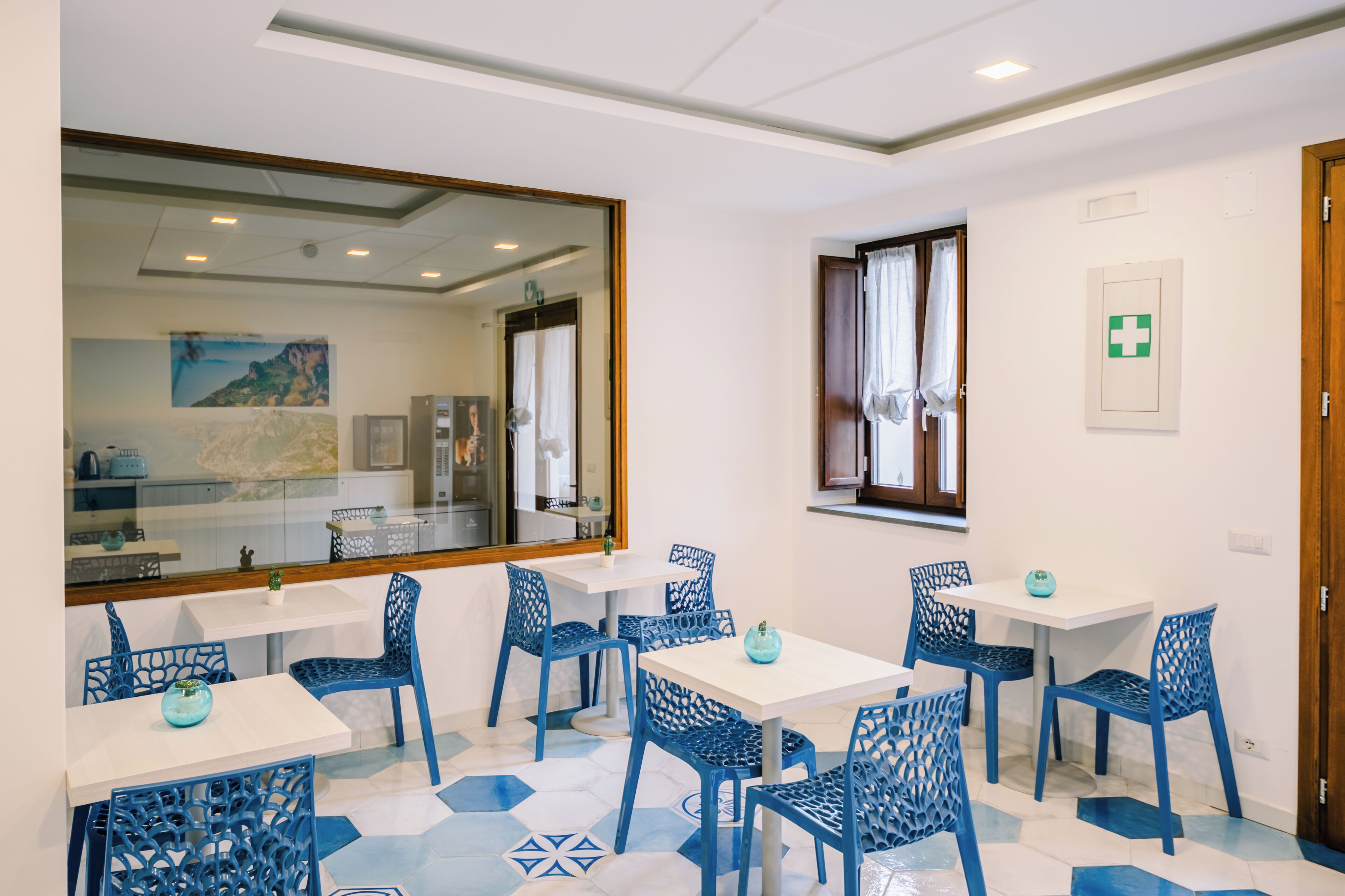 A room with white walls, a large mirror, and blue chairs around white tables.