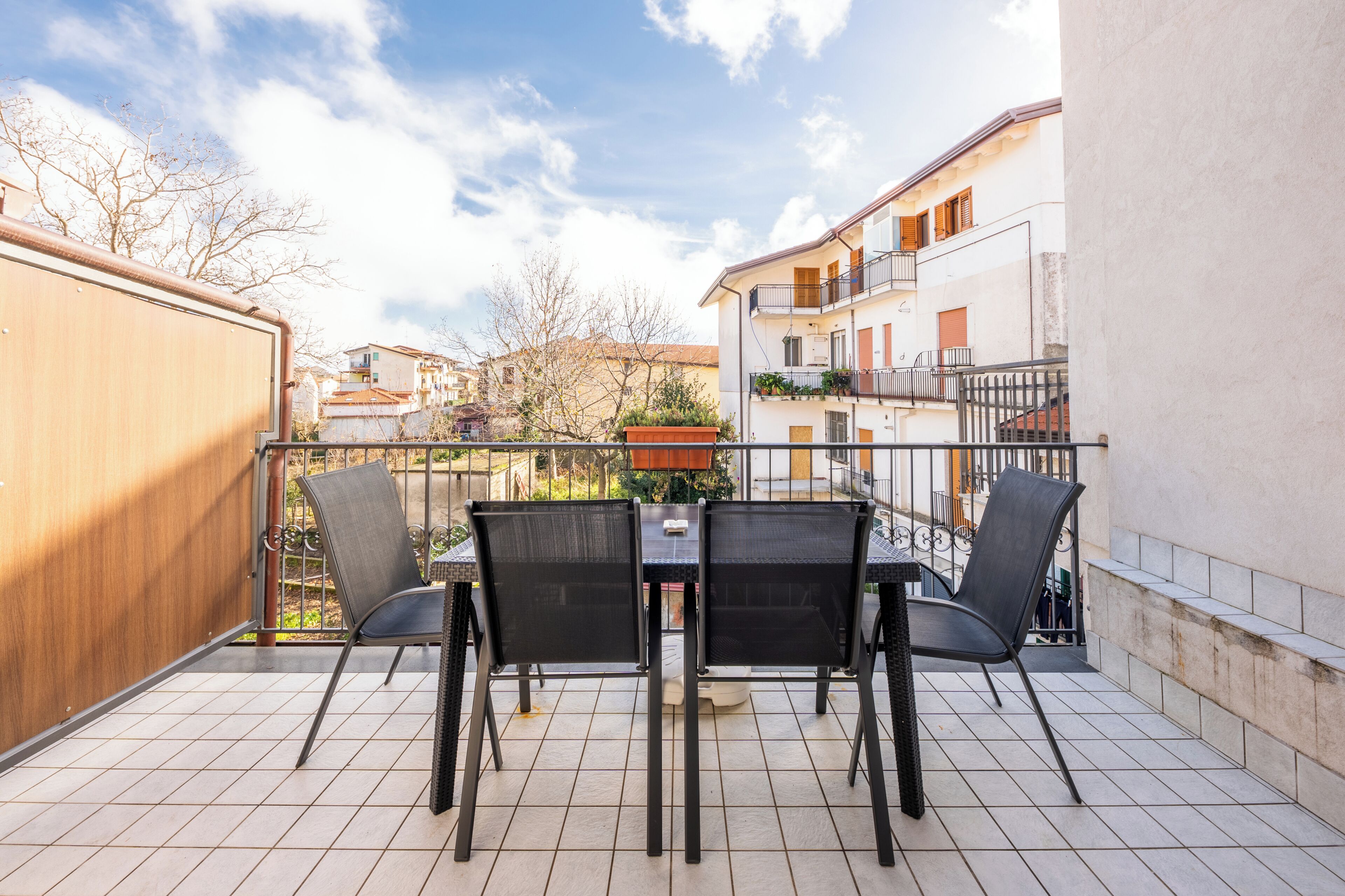 Un balcón con mesa y sillas, vista del barrio y un edificio con balcones.