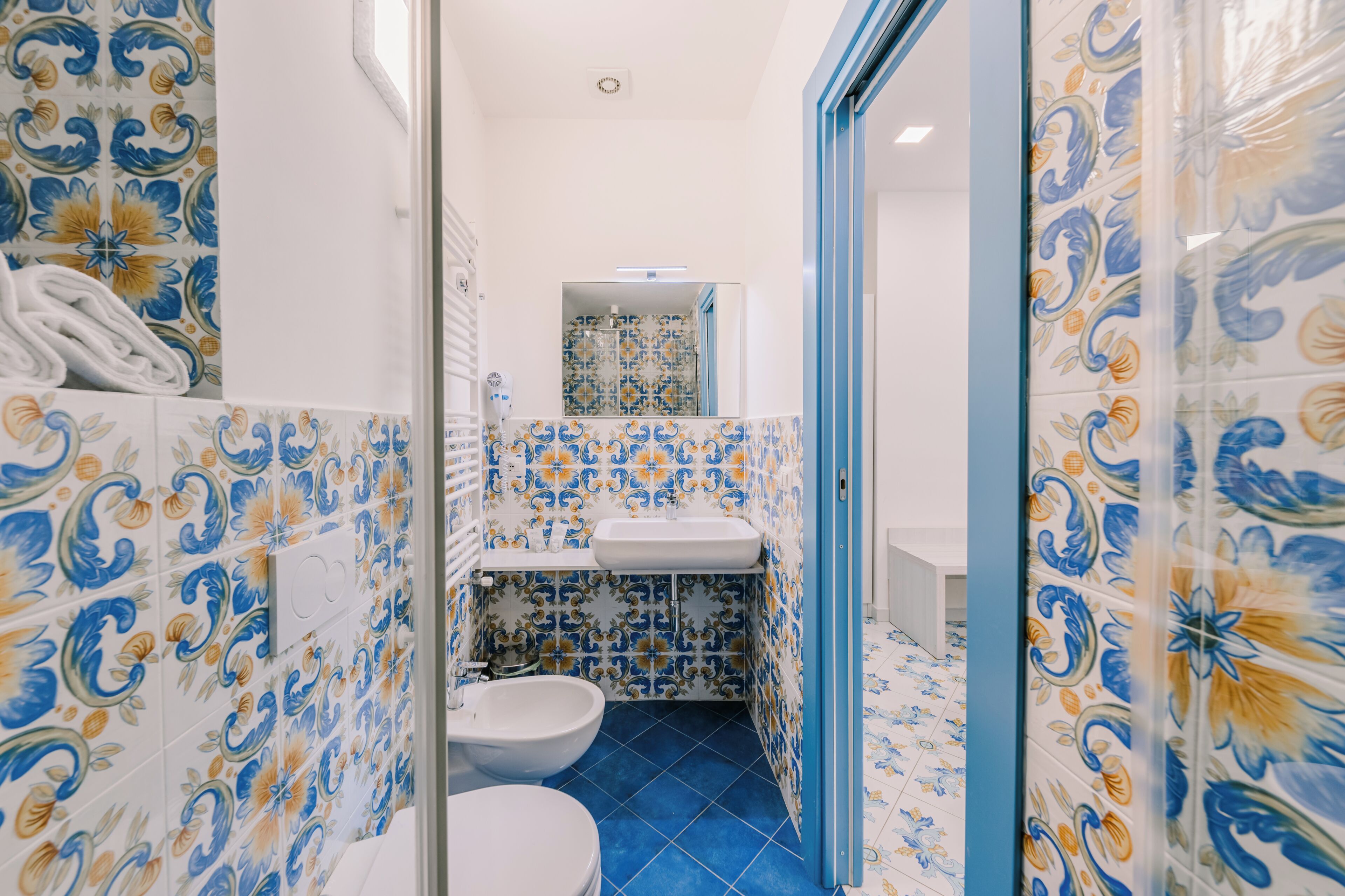 Une salle de bain comprenant des toilettes, un lavabo et un espace douche, avec des carreaux bleus et blancs aux motifs décoratifs.