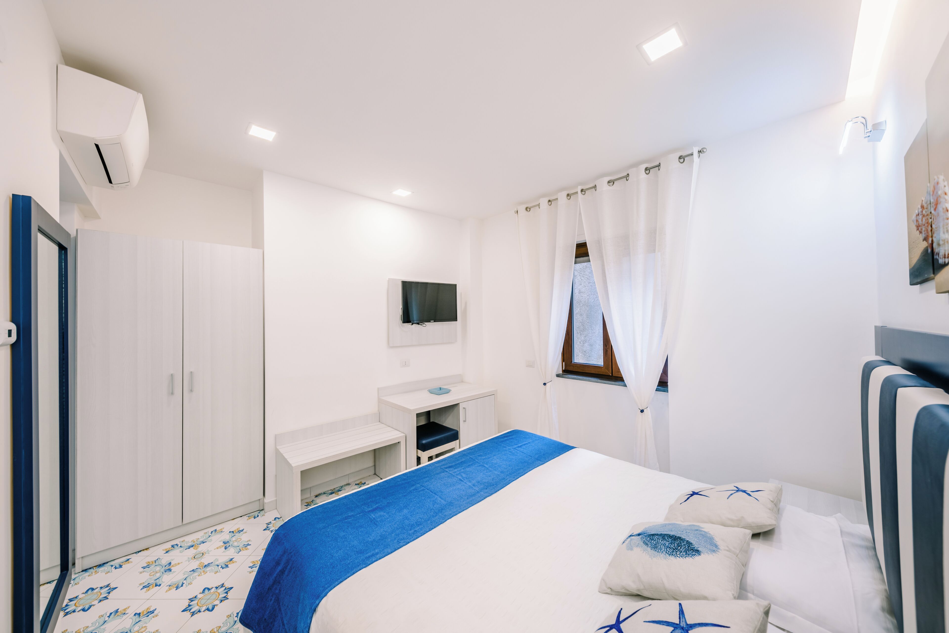 A hotel room with a bed, a desk, a TV, and a window with curtains.