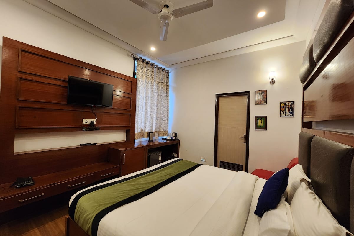 Une chambre d’hôtel comprenant un lit, une tête de lit en bois, un téléviseur, un bureau et une armoire.