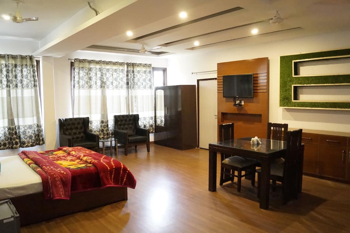 Une chambre d’hôtel comprenant un lit, un téléviseur fixé au mur, une table à manger avec des chaises et un buffet en bois.