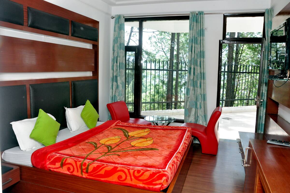 Une chambre d’hôtel avec un lit, un bureau, une chaise et une fenêtre donnant sur des arbres.