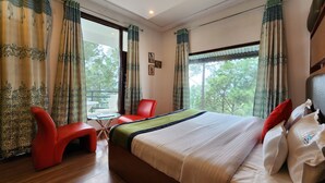 A hotel room with a bed, red chairs, a small table, and large windows with curtains. - Hotel Bliss (Kasauli)