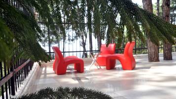 A modern outdoor seating area with red chairs and a glass table, surrounded by greenery and a metal fence.