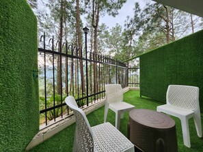 Een balkon met witte stoelen en een ronde tafel, omringd door groen kunstgras en een metalen hek.