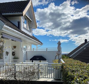 A white house with a balcony, a barbecue grill, and a view of the sky.