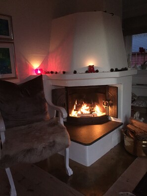A room with a fireplace, a white armchair, and a small table with a candle.