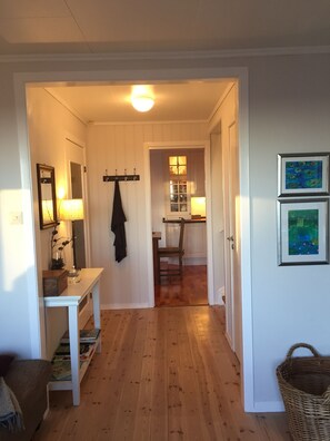 A hallway with a wooden floor, a coat rack, a table with a lamp, and a basket.