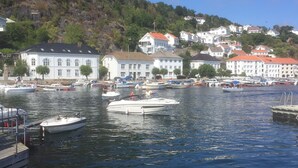 A marina with several boats docked, surrounded by white buildings with red roofs, set against a backdrop of a hill with greenery. - Idyllic southern country house in Risør (Risør)