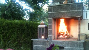 A stone fireplace with a visible fire, surrounded by greenery and a lantern. - Idyllic southern country house in Risør (Risør)