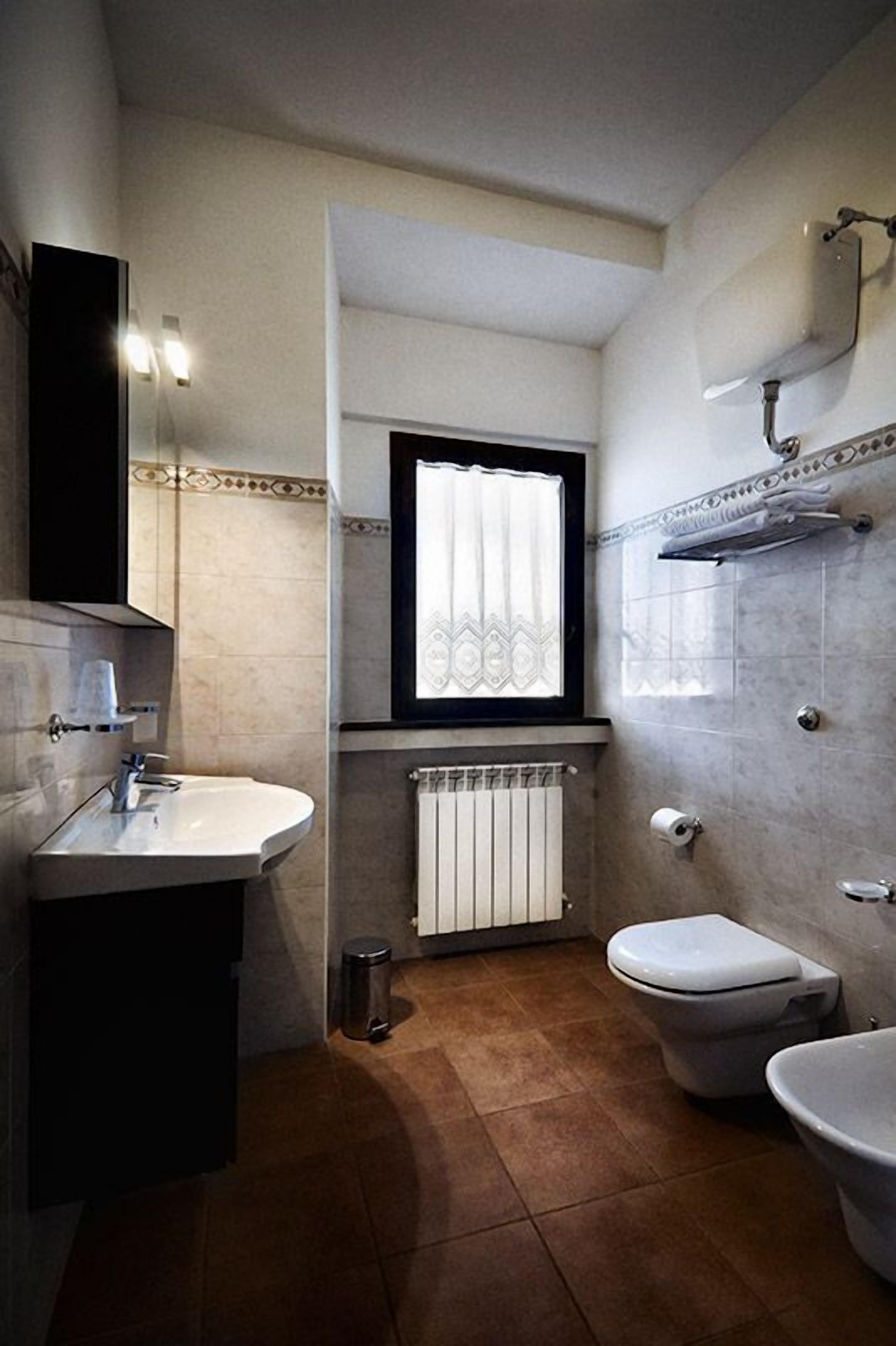 Un baño pequeño con un lavamanos blanco, un inodoro y una ventana con cortina.