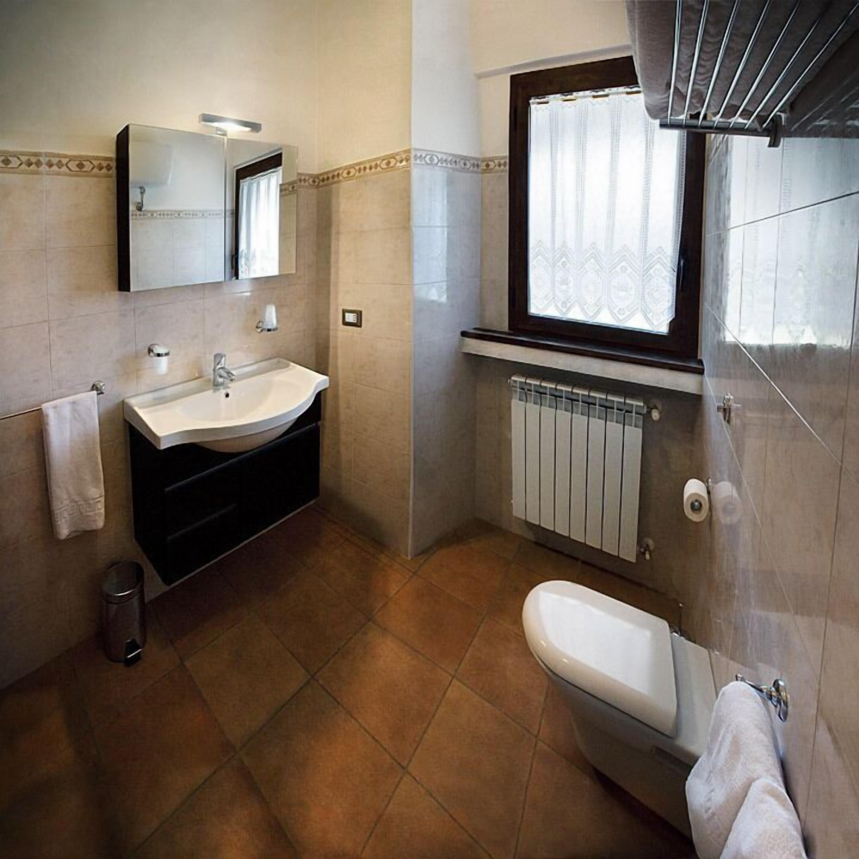 A bathroom with a sink, mirror, window, radiator, and bathtub.