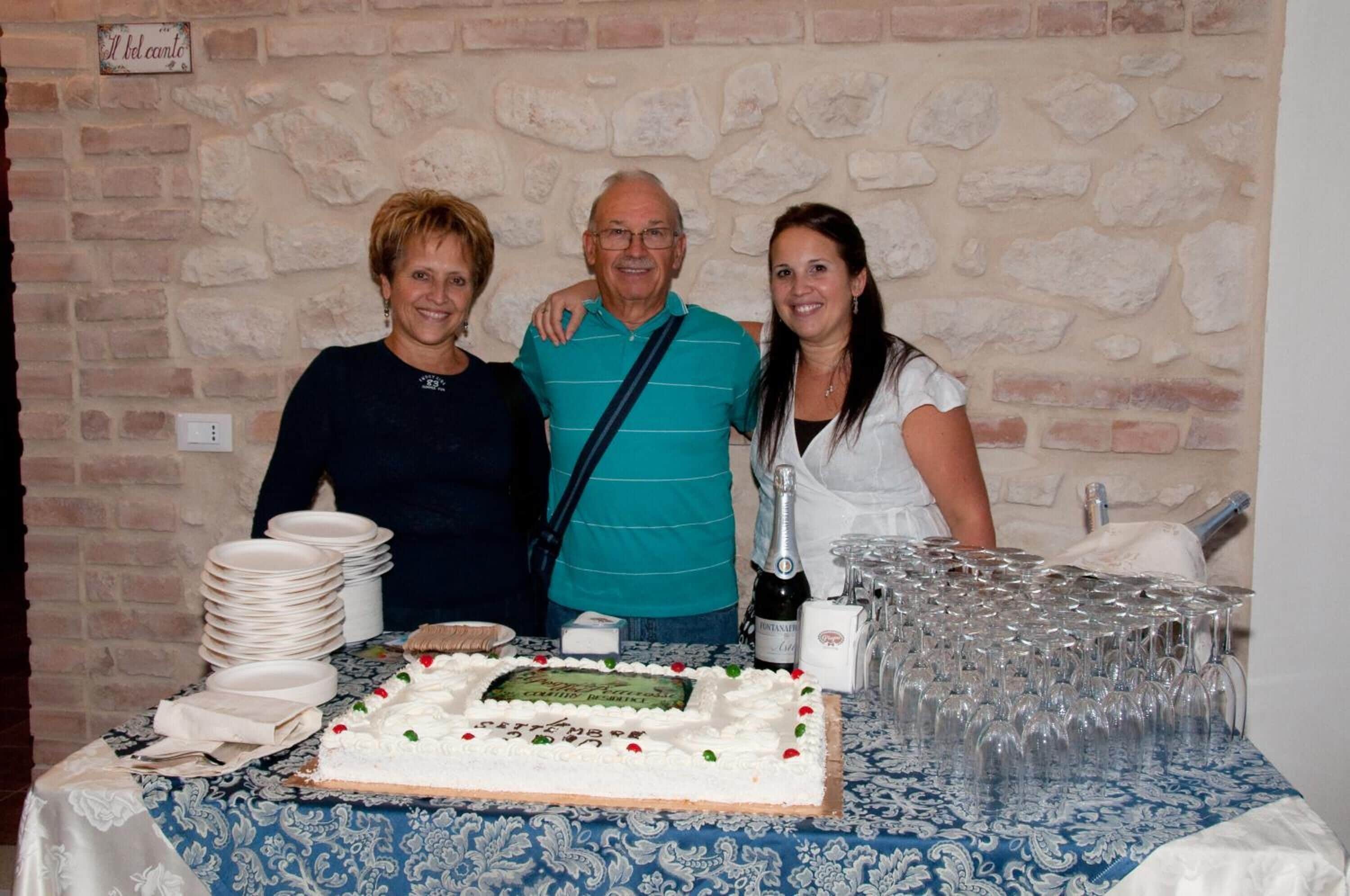 A table with a cake, plates, and glasses, set against a brick wall.