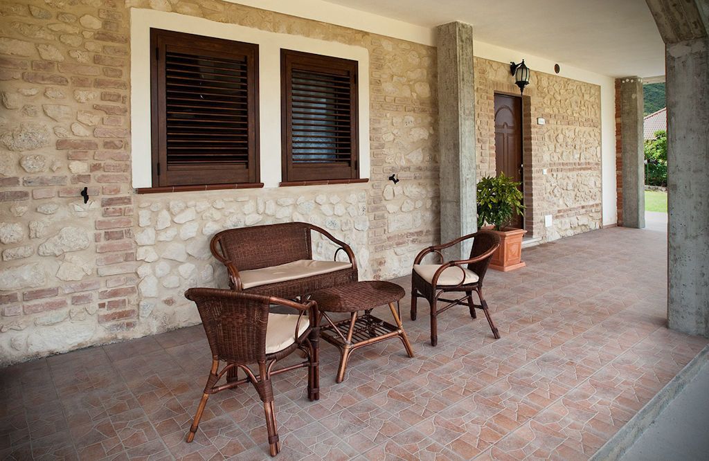 Un patio couvert aménagé avec des meubles en osier, des murs en pierre et une plante en pot.