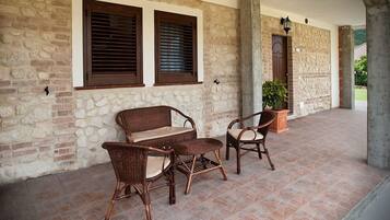 Un patio couvert aménagé avec des meubles en osier, des murs en pierre et une plante en pot.