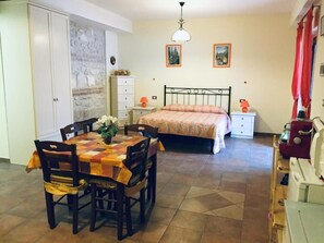 A room with a bed, a bedside table, a lamp, a dresser, a table with chairs, and a wall with a decorative pattern. - Il Poggio Dei Pettirossi (Pettorano sul Gizio)