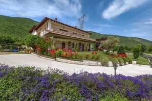Une maison à deux étages avec un porche, entourée d’un jardin aménagé avec différentes plantes et fleurs.