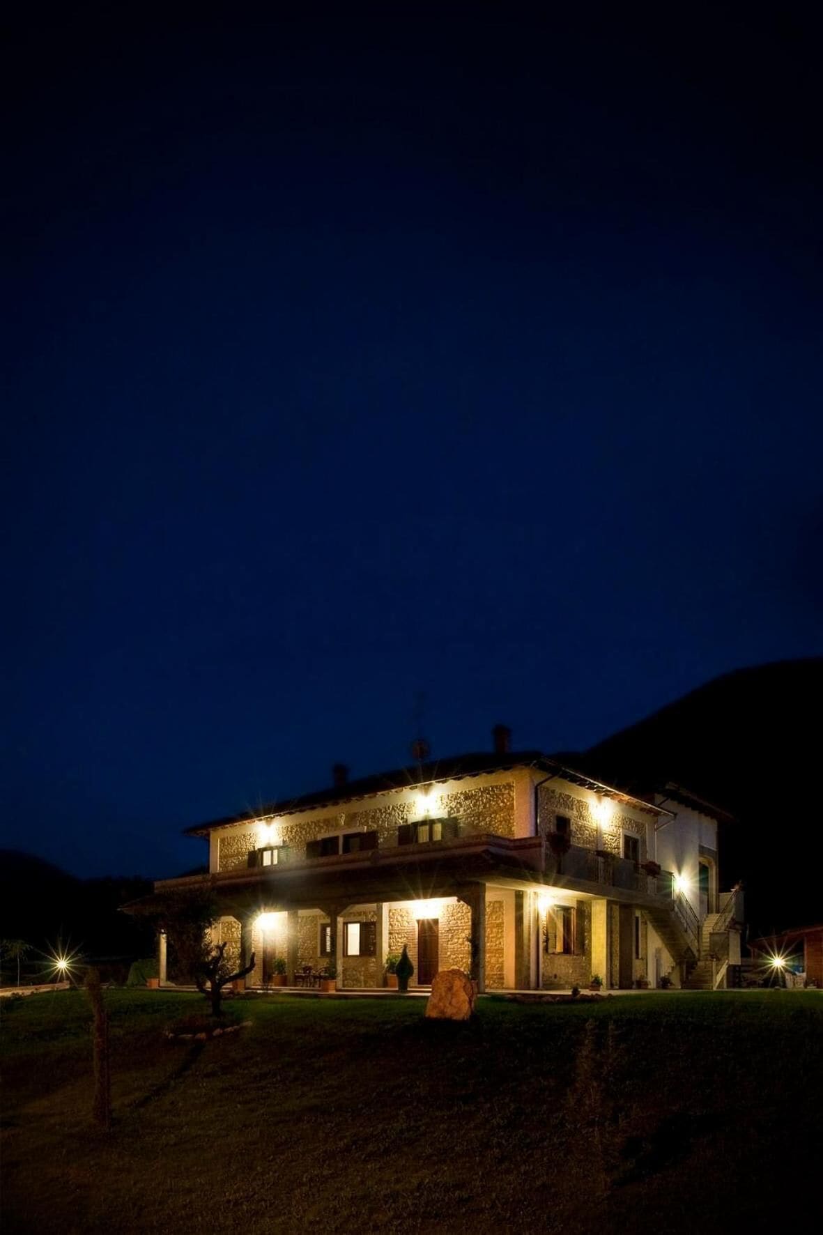 Ein zweistöckiges Gebäude mit Steinaußenwand, beleuchtet durch Außenlichter, vor dunklem Himmel.