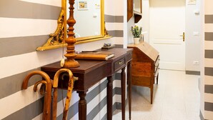 A hallway with a striped wall, a wooden desk with a lamp, a mirror, and a door. - Casa Dreosti (Cortona)