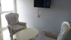 Una sala de estar con un televisor de pantalla plana montado en la pared, dos sillones y una mesita.