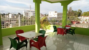 Un balcón con paredes verdes, piso de baldosas blancas y sillas rojas y verdes.