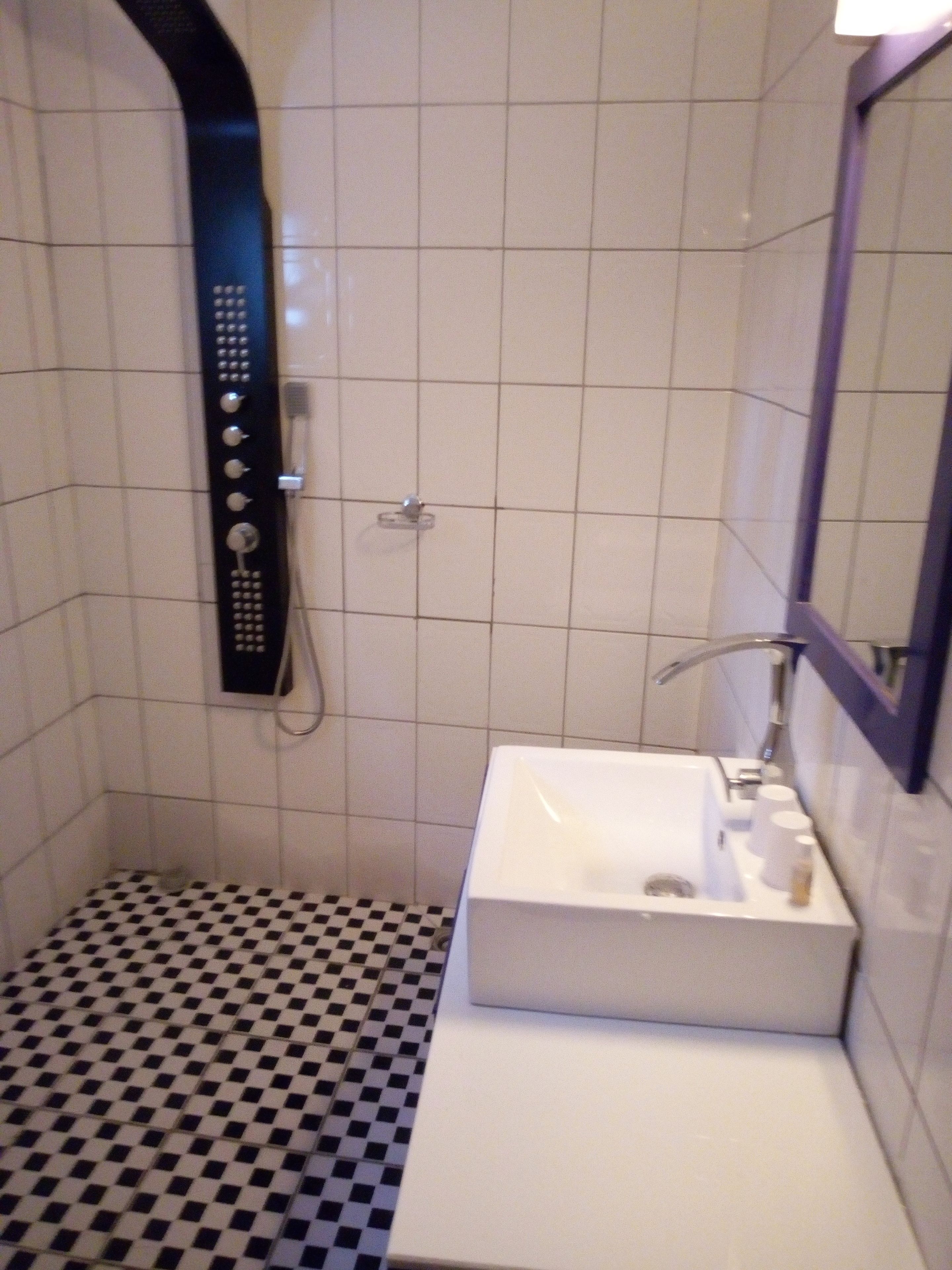 Un baño con piso a cuadros, un lavamanos blanco y una ducha con panel de control.