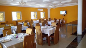 Un comedor con varias mesas y sillas, una araña y un televisor en la pared.