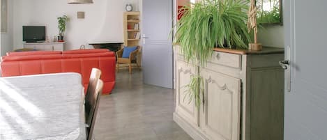 A living room with a red sofa, a dining table, and a cabinet with plants.