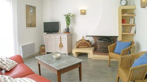 Ein Wohnzimmer mit einem roten Sofa, einem Korbsessel, einem Kamin und einem Fernseher auf einem Schrank.