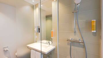 Un baño moderno con ducha de vidrio, lavamanos blanco y rollo de papel higiénico a la vista.