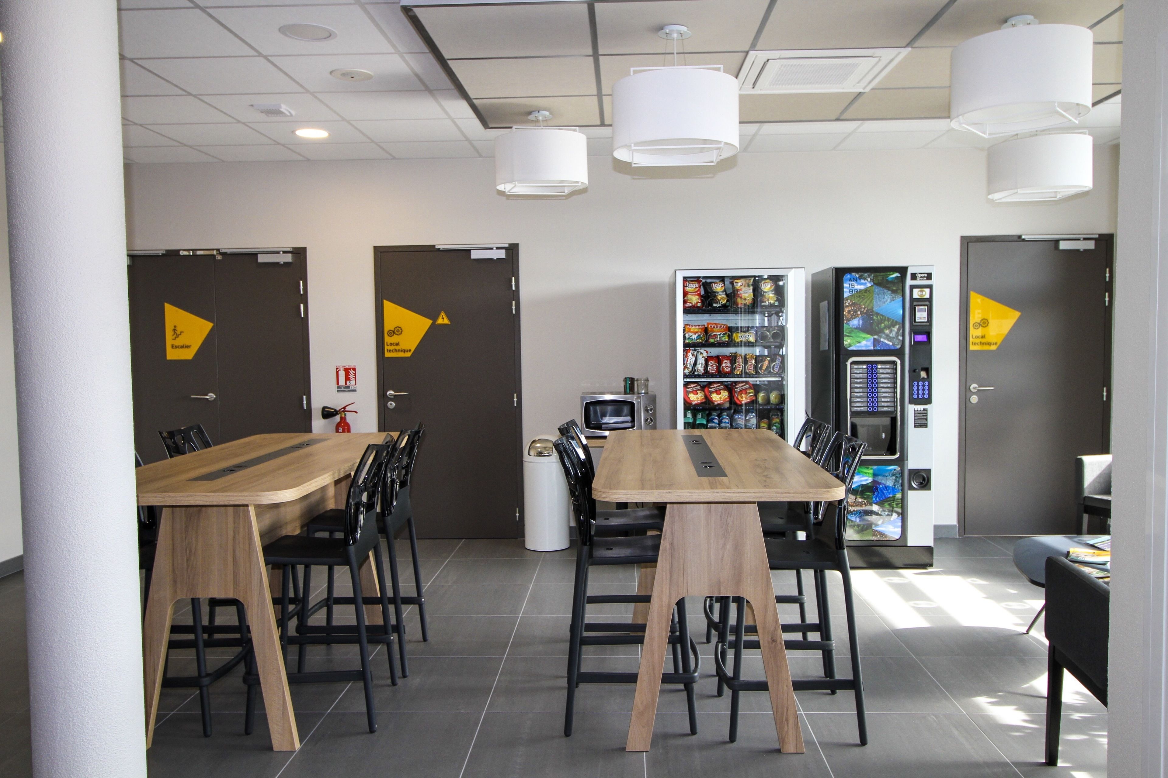 A modern dining area with a wooden table and black chairs, a vending machine, and a microwave.