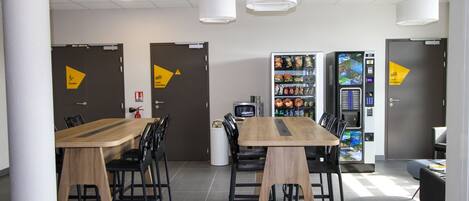 A modern dining area with a wooden table and black chairs, a vending machine, and a microwave.