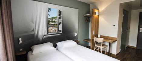A hotel room with a bed, a desk, a chair, and a window with a view of a rocky landscape.