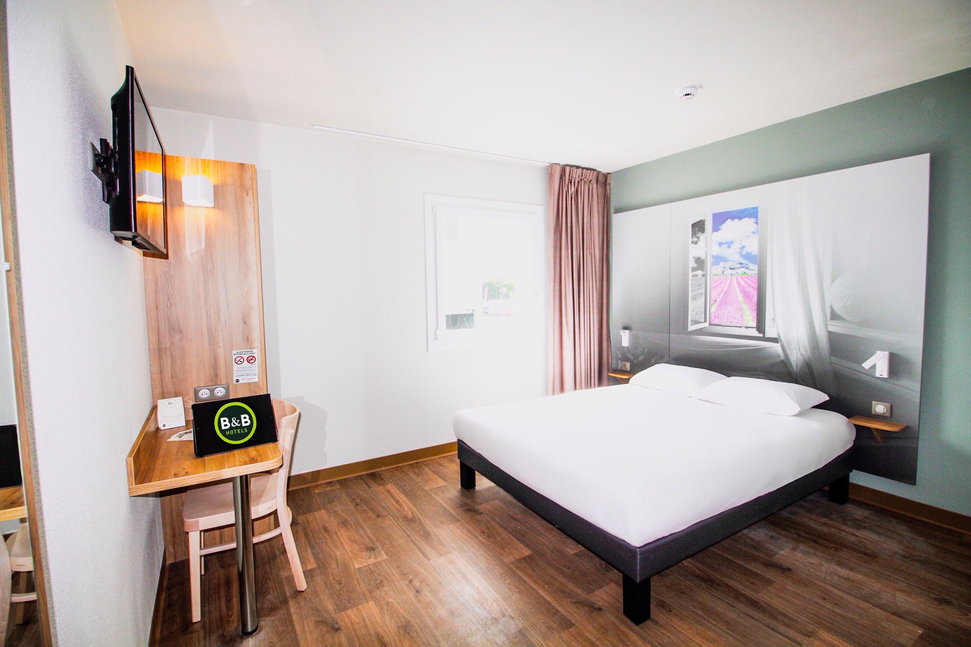 Una habitación de hotel con un escritorio de madera, una cama y un espejo grande en la pared.