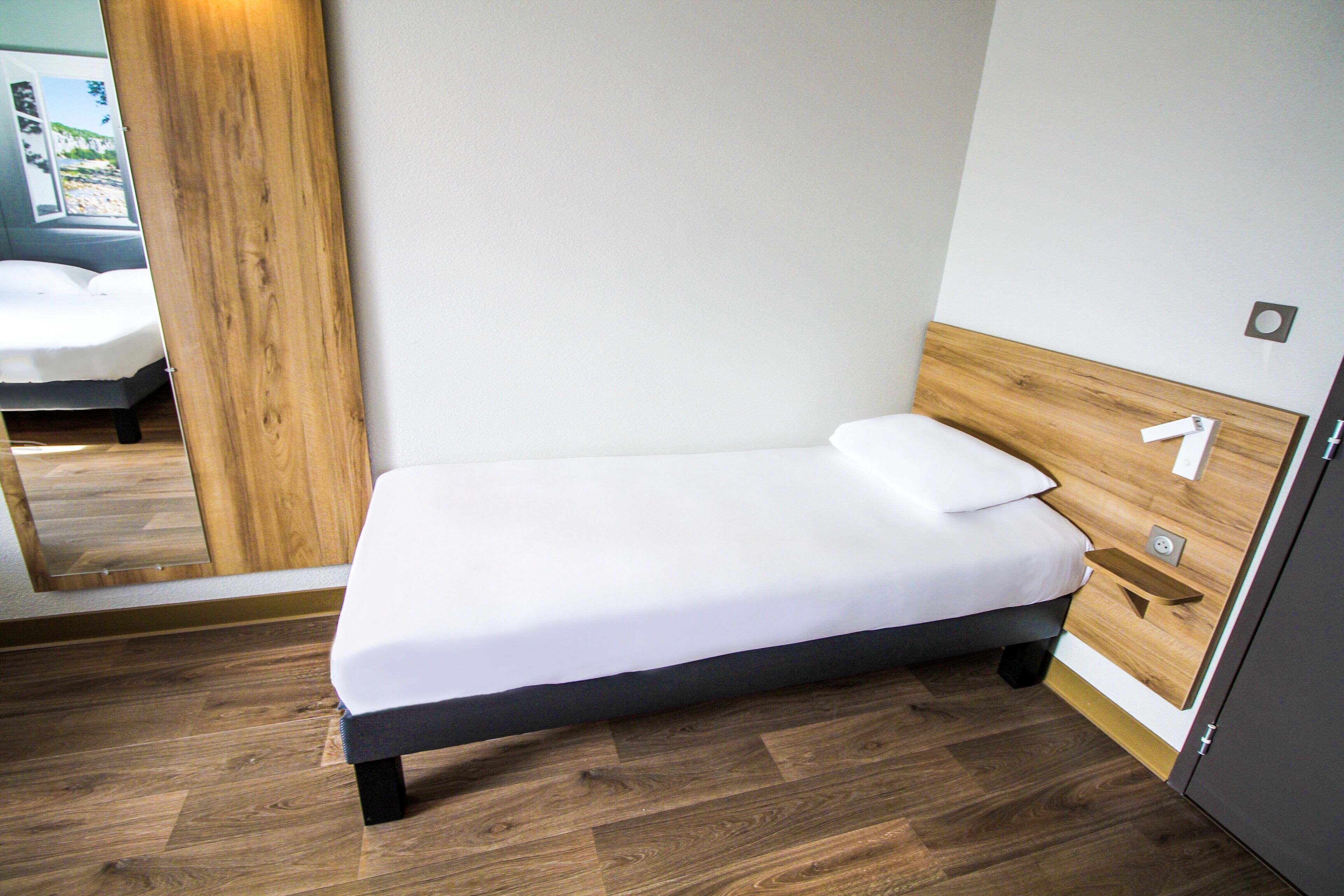 A small, single-bed room with a wooden headboard, a bedside table, and a mirror.