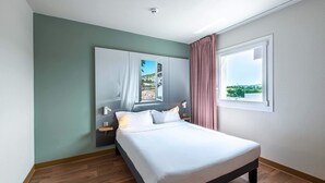 A bedroom with a bed, a nightstand, a window with curtains, and a painting on the wall.