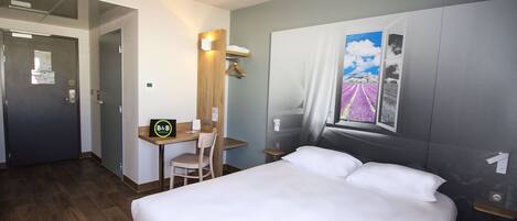 Habitación de hotel con cama, escritorio con silla, ventana con vistas a campos de lavanda y una puerta.