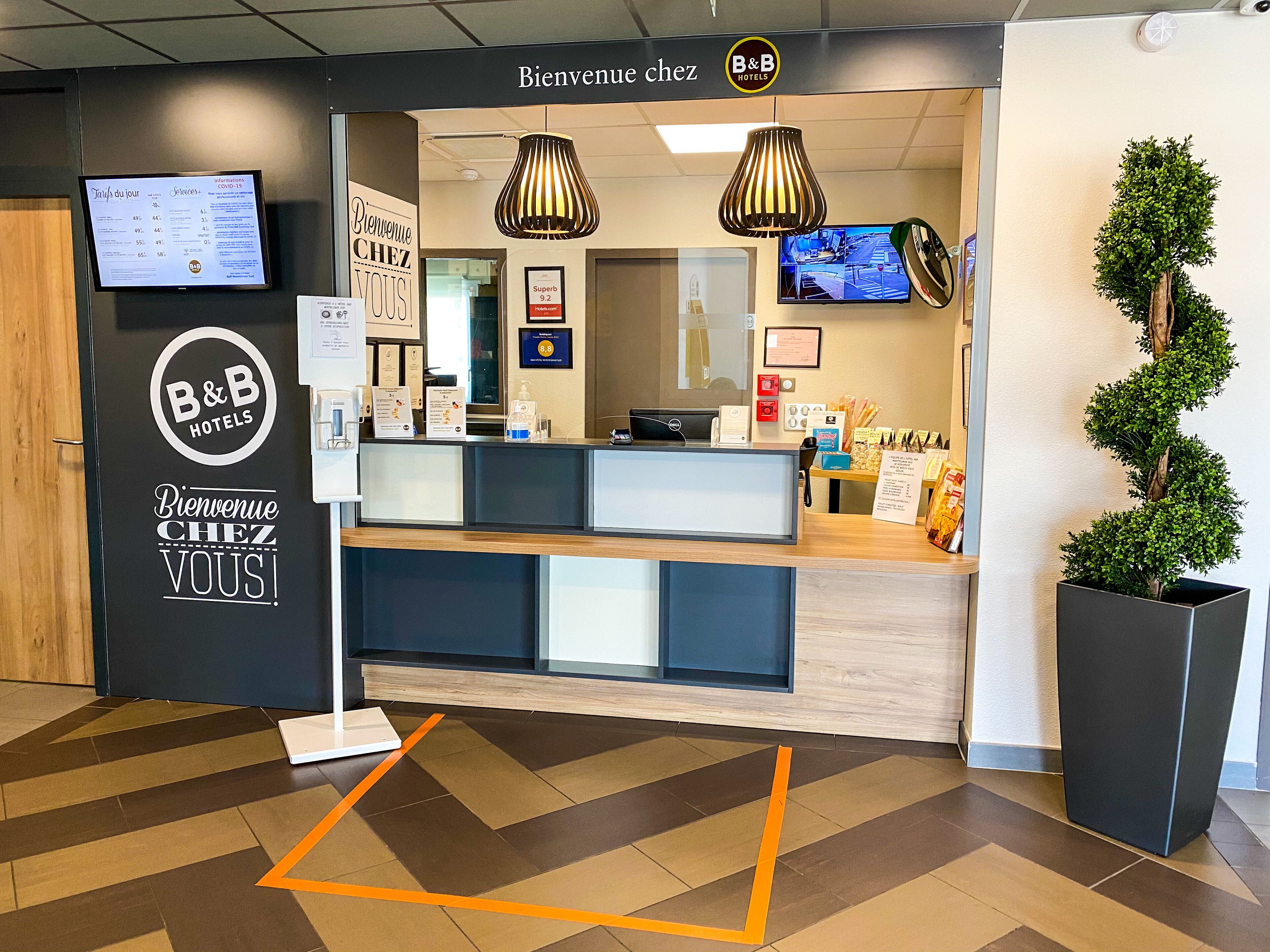 Un espace d’accueil avec une enseigne B&B Hotels, un écran numérique et un comptoir de réception.