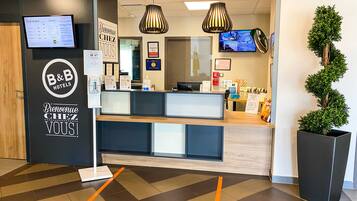 Un espace d’accueil avec une enseigne B&B Hotels, un écran numérique et un comptoir de réception.