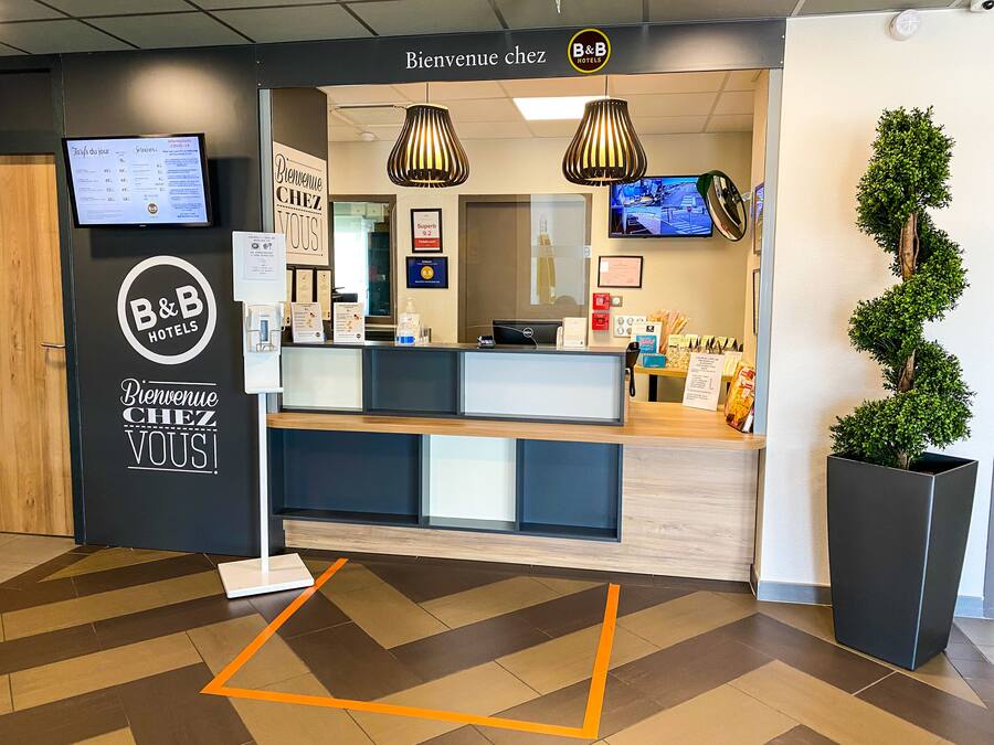 Un espace d’accueil avec une enseigne B&B Hotels, un écran numérique et un comptoir de réception.