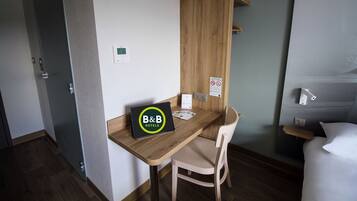 A hotel room with a wooden desk, a laptop with 'B&B HOTELS' logo, a bed, and a bedside table.