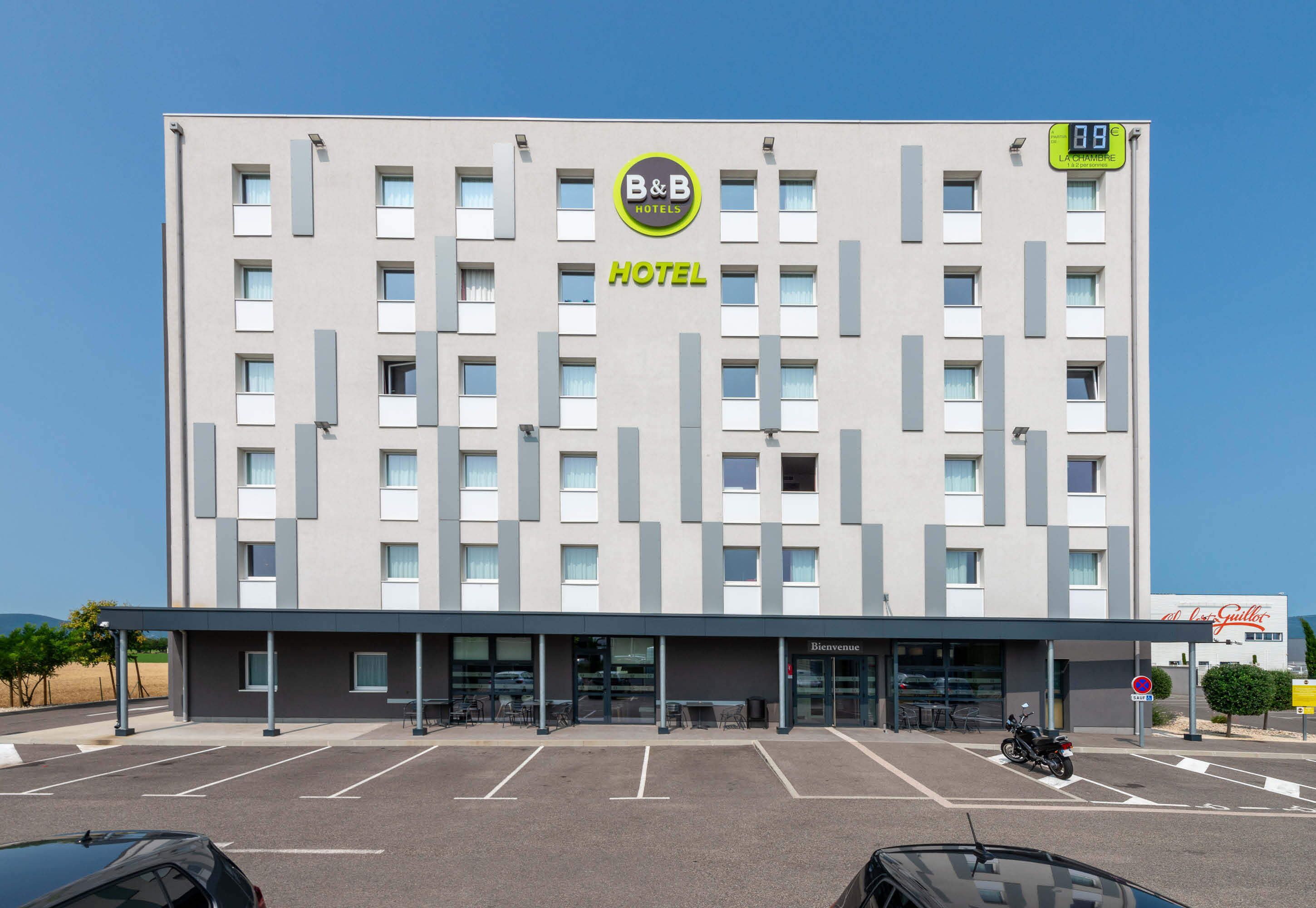 Et Bed and Breakfast hotel med en moderne facade, en parkeringsplads og et skilt, der angiver værelsespriser.