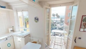 A compact kitchen with a dining area, a view of the street, and a balcony with a table and chairs. - Lovely 2P in Menton with sea view and terrace (Menton)