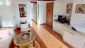 A compact living space with a kitchenette, a dining area with a glass table, and a sofa. There is a wooden door and a wall-mounted light fixture. - Lovely 2P in Menton with sea view and terrace (Menton)