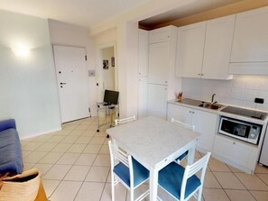 A compact kitchen with white cabinets, a dining table with blue chairs, a microwave, and a small TV on a stand. - 2-room apartment with terrace and private garage in Menton (Menton)