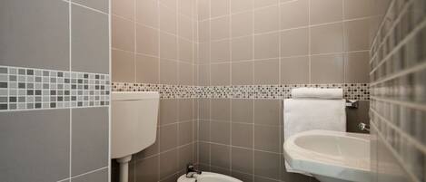 Un baño con inodoro, bidé y lavabo, con azulejos en tonos neutros.