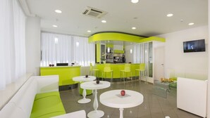 Eine moderne Hotelhalle mit weißen Sofas, grünen Akzenten und einer gebogenen Bar.