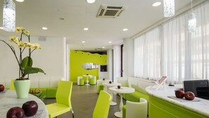 Eine moderne Hotelhalle mit leuchtend grünen Sitzgelegenheiten, einem Empfangstresen und einem großen Fenster mit Vorhängen.