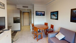 Un salon moderne comprenant un canapé, une table à manger avec des chaises, un téléviseur et un coin cuisine avec des placards et un four à micro-ondes.